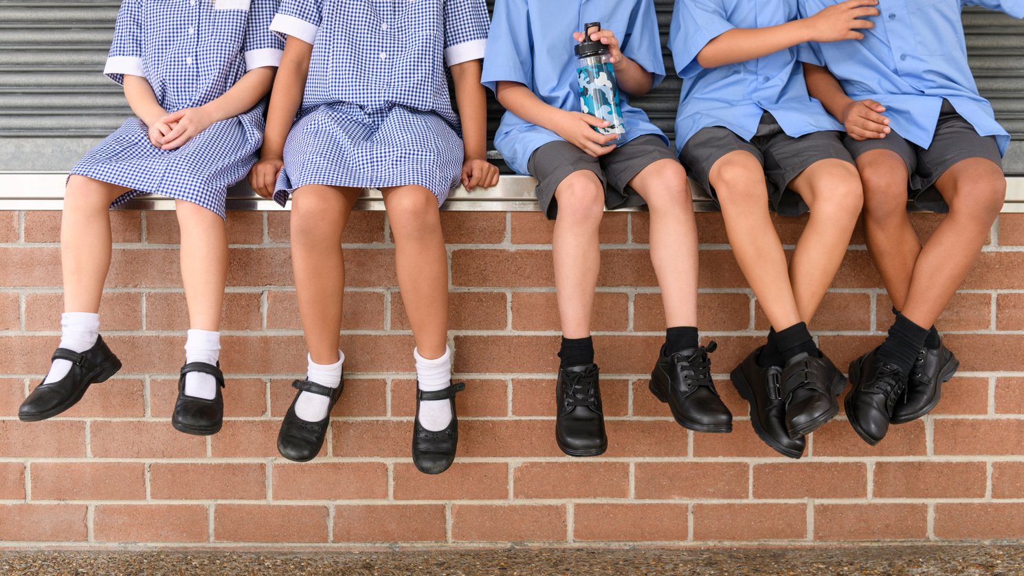 Low section view of five school children sitting on brick wall wearing school uniform